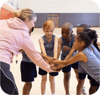 Female teacher coaching group of diverse children basketball.