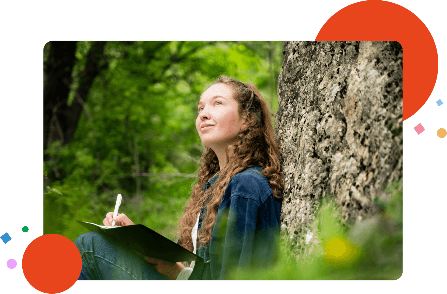 Dreamy young woman with curly hair writing something in notebook outdoors looking up relaxing resting alone keeping diary journaling dressed casual dark blue shirt sitting in nature park, portrait