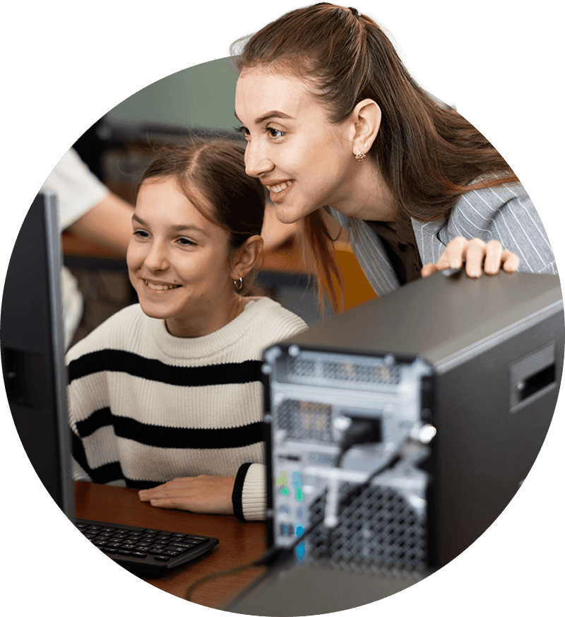 Smiling female teacher talking to happy teenage girl student sitting at computer in classroom, praising successful completion test