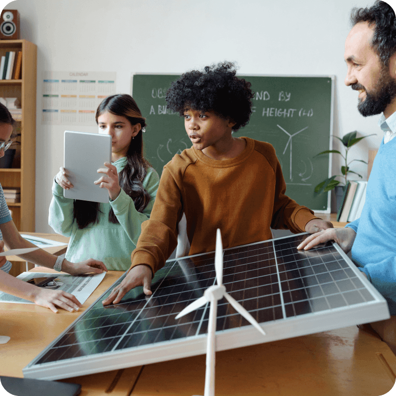 Group of diverse children and teacher working in classroom on solar energy project with wind turbines, discussing and collaborating on renewable energy concepts