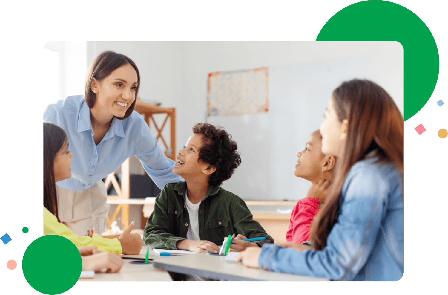 Happy diverse kids sitting at desk in classroom and talking with teacher, studying during lesson, woman explaining subject to pupils